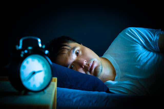 Man lying awake in bed at night, alarm clock at 2.40am