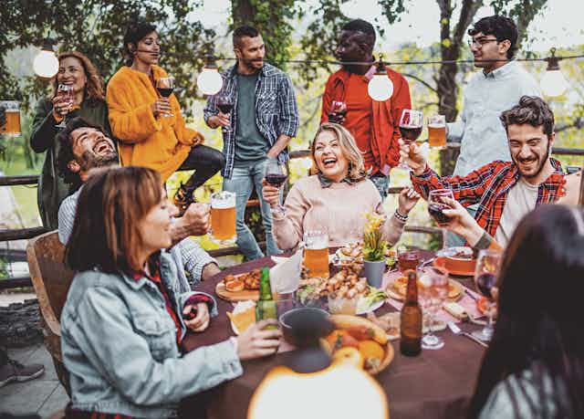 Un grupo de adultos ríen alrededor de una mesa de patio mientras disfrutan de bebidas alcohólicas.