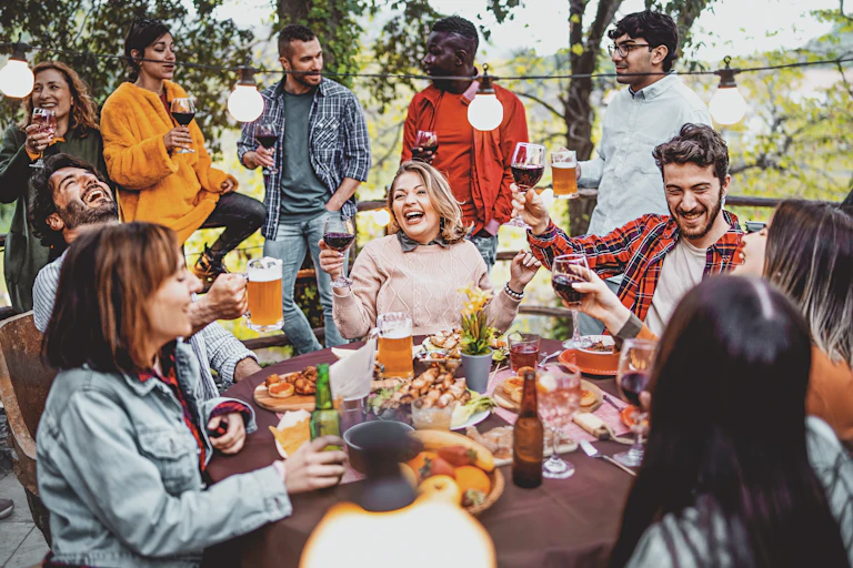 Un grupo de adultos ríen alrededor de una mesa de patio mientras disfrutan de bebidas alcohólicas.