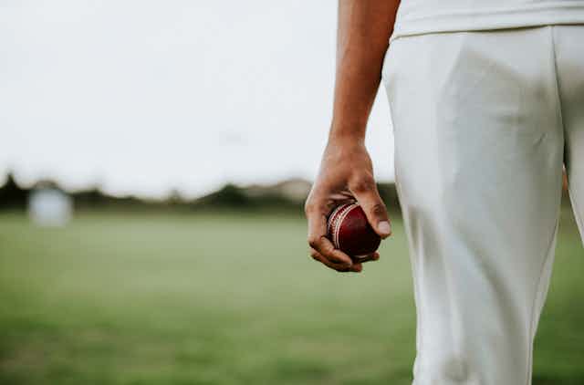 Close up of a hand holding a red cricket ball.