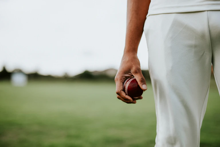 Close up of a hand holding a red cricket ball.