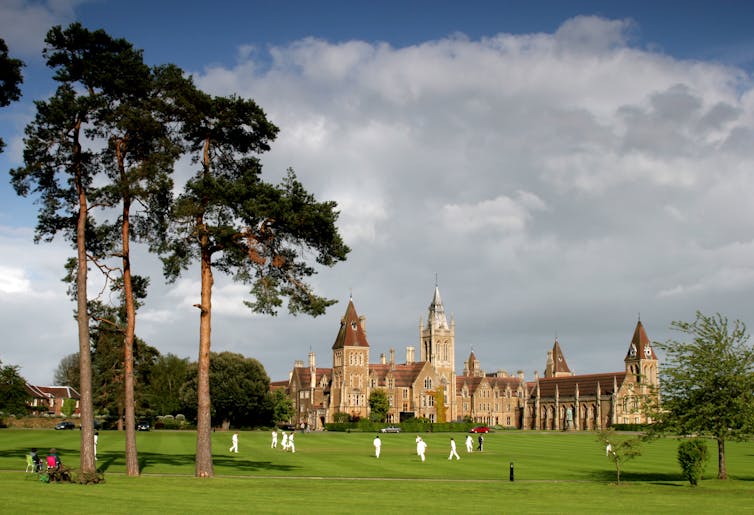Boys playing cricket in the grounds of a grand private school.