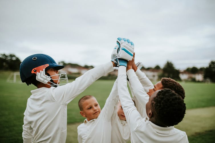 A group of children in cricket whites high-fiving each other.