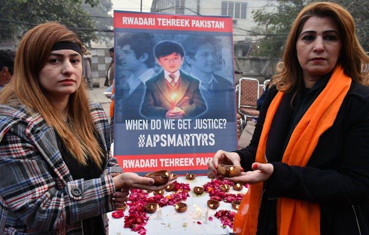 امرأتان تحملان ملصقاً تخليداً لذكرى الأطفال الذين ماتوا.