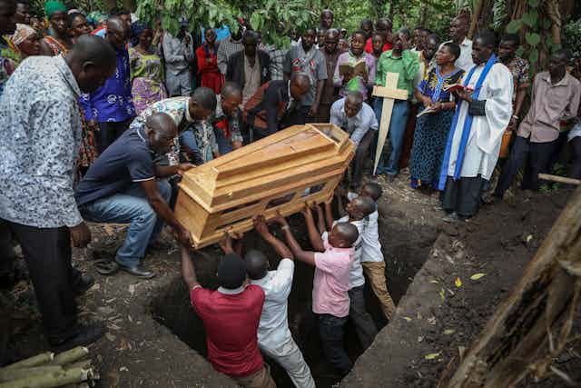 Men lowering a coffin into its burial space.