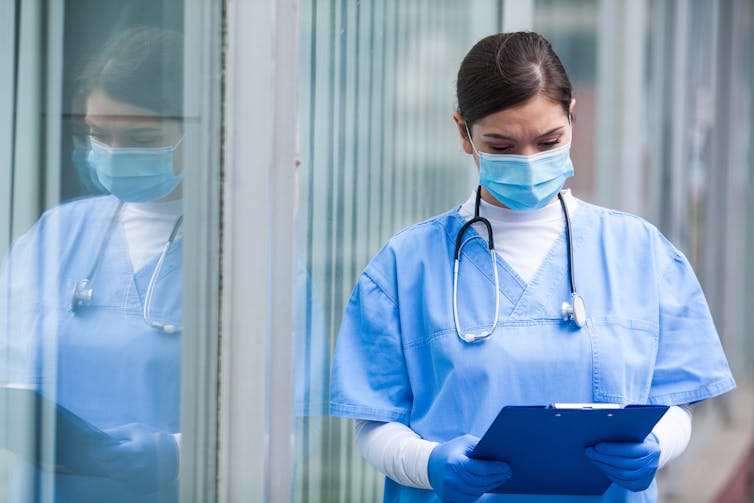 A healthcare worker wearing PPE looks at a clipboard.