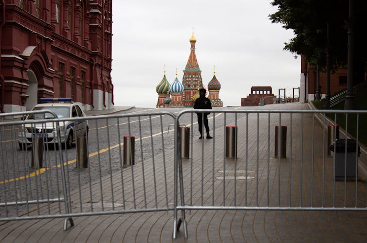 A large street and sidewalk barred by barricades, with onion-domed buildings in the background.