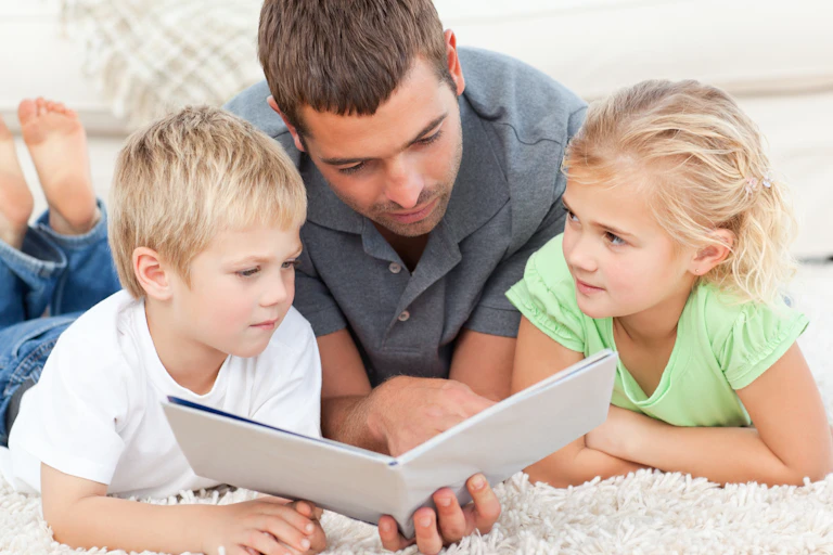 A man reading to his two children, boy and a girl.