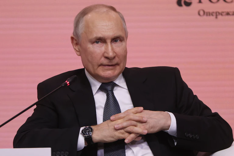 A man with thinning hair, black jacket and white shirt, talking into a microphone and looking tentative.