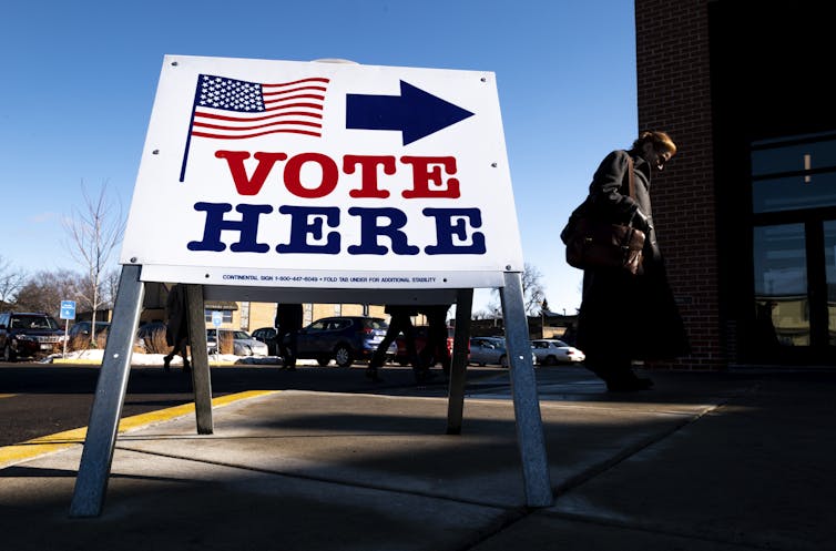 A person walks past a white sign that says 'Vote here.'