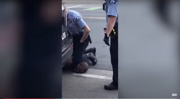 A uniformed, white police officer kneels on the neck of a Black man as he lies on the ground.