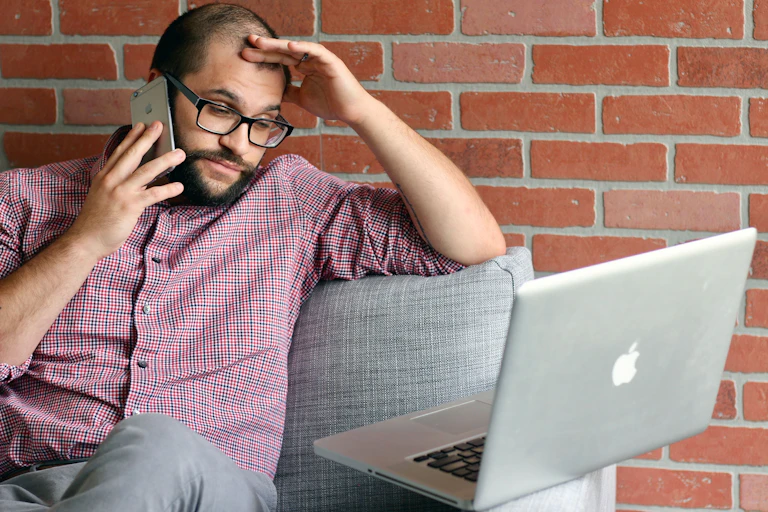 a frustrated man makes a phonecall while he's looking at a laptop