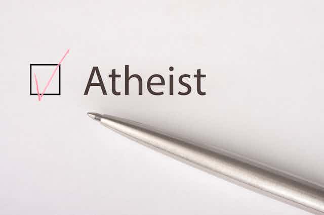A silver pen sits on a piece of paper that says 'atheist,' and the box next to the word has a red check in it.