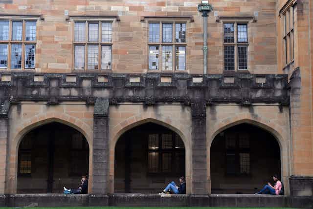 Three students sit in the quadrangle at Sydney University. 