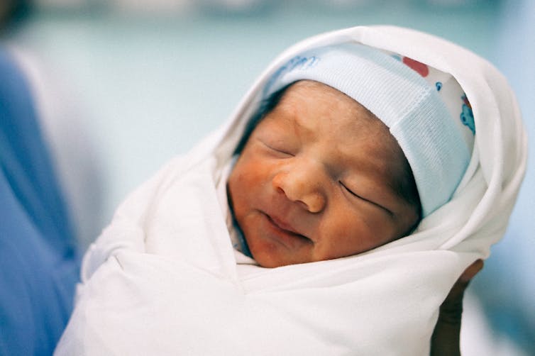 A photo of a sleeping newborn baby wrapped up in swaddling.