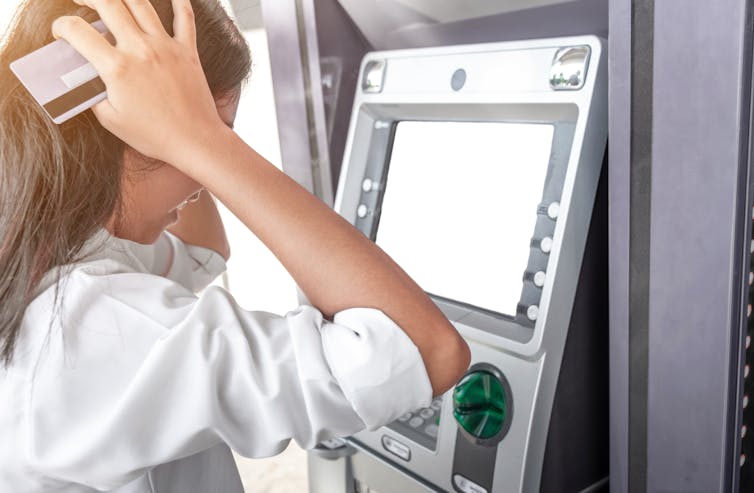 Woman looks at the ATM in despair as she realises her bank account is empty.