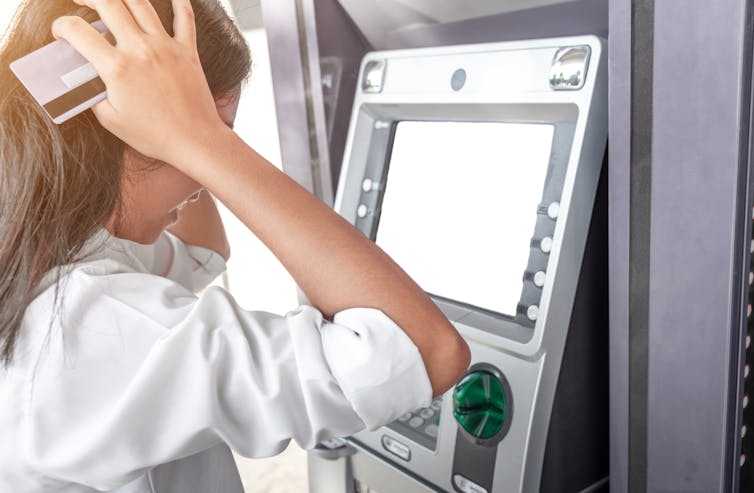 Woman looks at the ATM in despair as she realises her bank account is empty.