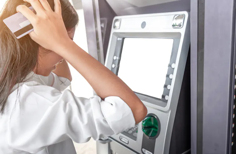 Woman looks at the ATM in despair as she realises her bank account is empty.