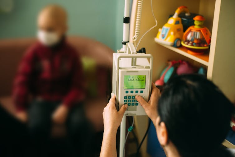 child with bald head in blurred in background of medical setting with toys on shelf