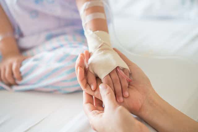 child with IV line in holds adult hand