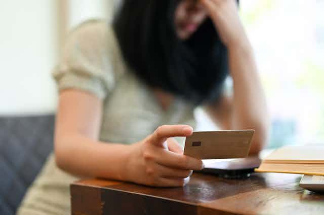 Woman looks at her credit card, holding her head in despair.