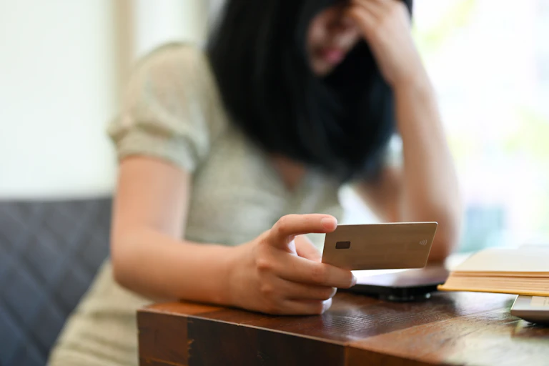 Woman looks at her credit card, holding her head in despair.