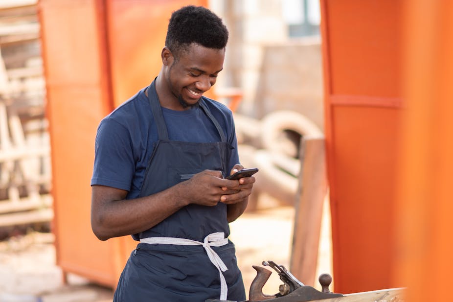 A young man grins at the cellphone he is holding in both hands