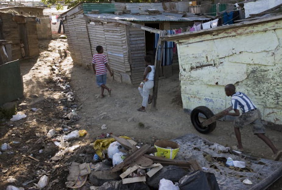 A boy pushes a tyre among dirt in a shack land. 