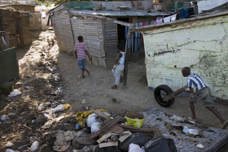 A boy pushes a tyre among dirt in a shack land.