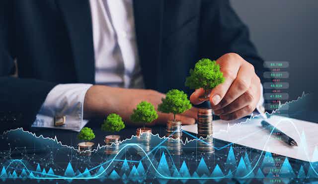 Person in suit holding coin with tree growing on coin stack and digital growth graph.