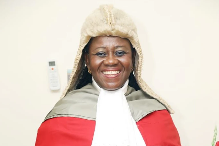 A smiling woman wearing a wig and a gown