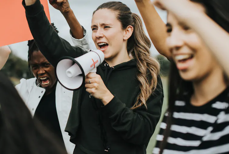Woman with megaphone surrounded by other people with arms raised.