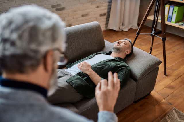 man lies on therapist's couch while person talks to him