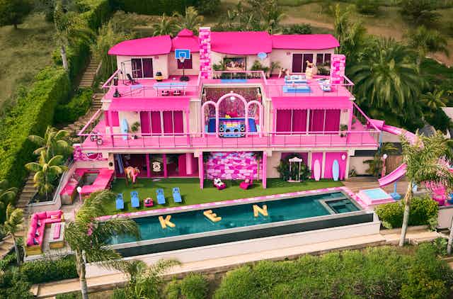 A pink Barbie Dream House in Malibu with pool floats outside spelling the word 'KEN'.