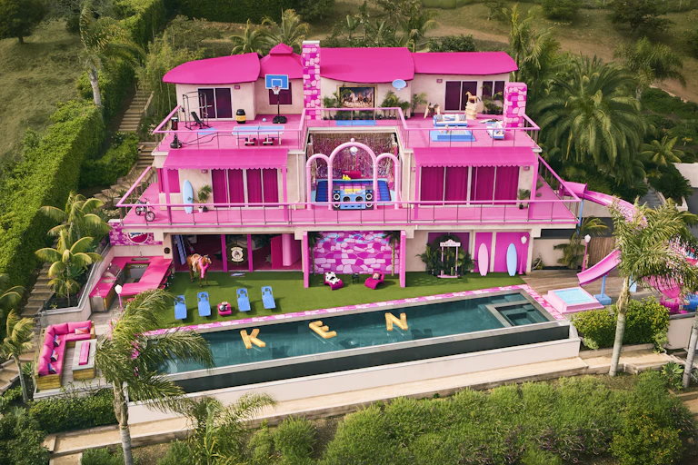 A pink Barbie Dream House in Malibu with pool floats outside spelling the word 'KEN'.