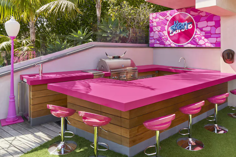 the grill area with pink table and chairs and Ken's logo graffitied over Barbie's.