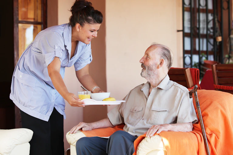 Carer bringing tray of food to elderly man.