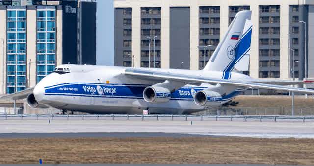 A large blue and white cargo plane that says Volga Dneper on its side sits on an airport tarmac.