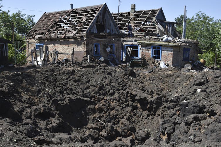 A large crater of dirt and rubble next to damaged houses.