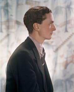 Edward James photographed side on, against a pale pastel patterned backdrop.