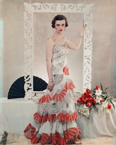 Margaret Sweeny in a frilly white and red dress, stands holding a frame.