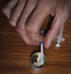 A person's hand seen using a fentanyl test strip to test a dose of heroin in a small container