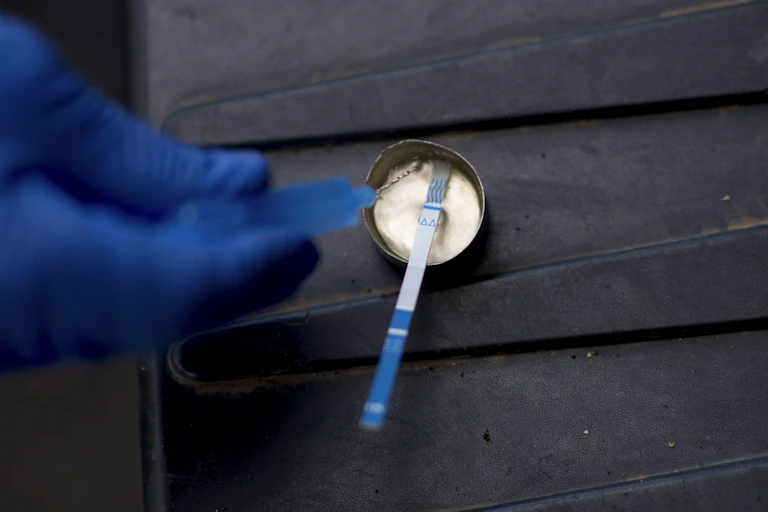 A gloved hand uses a test strip to test drugs in a small metal cup