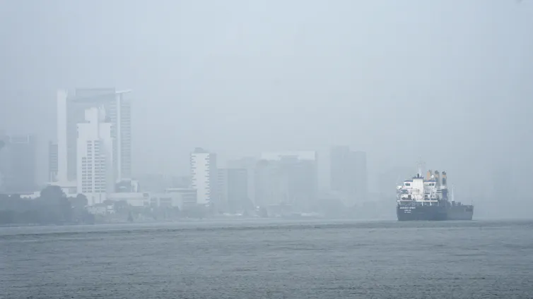 A freighter passes through a river as smoke fills the sky reducing visibility.