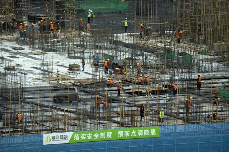 Construction workers at a construction site with a green sign with Chinese characters in front of them.