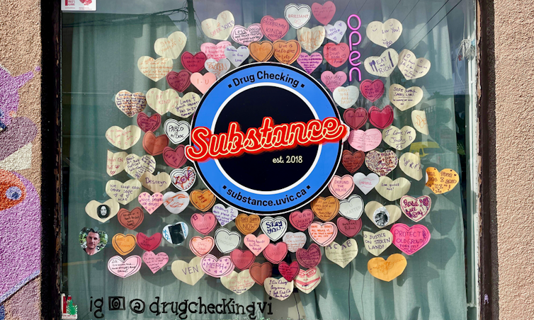 A window with a logo in a circle reading Substance, est. 2018, surrounded by paper hearts with handwritten messages.