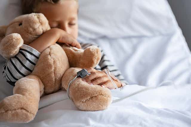 A child in a hospital bed holding a teddy bear.