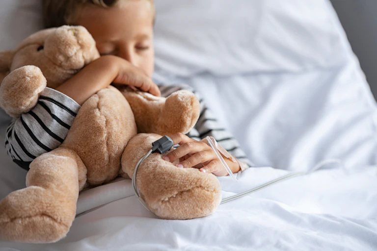 A child in a hospital bed holding a teddy bear.