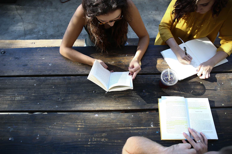 Three young people look at books on a bench.