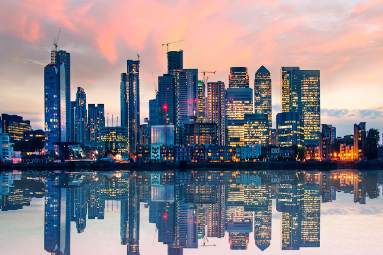 Buildings and skyscrapers reflected in a river at sunset.